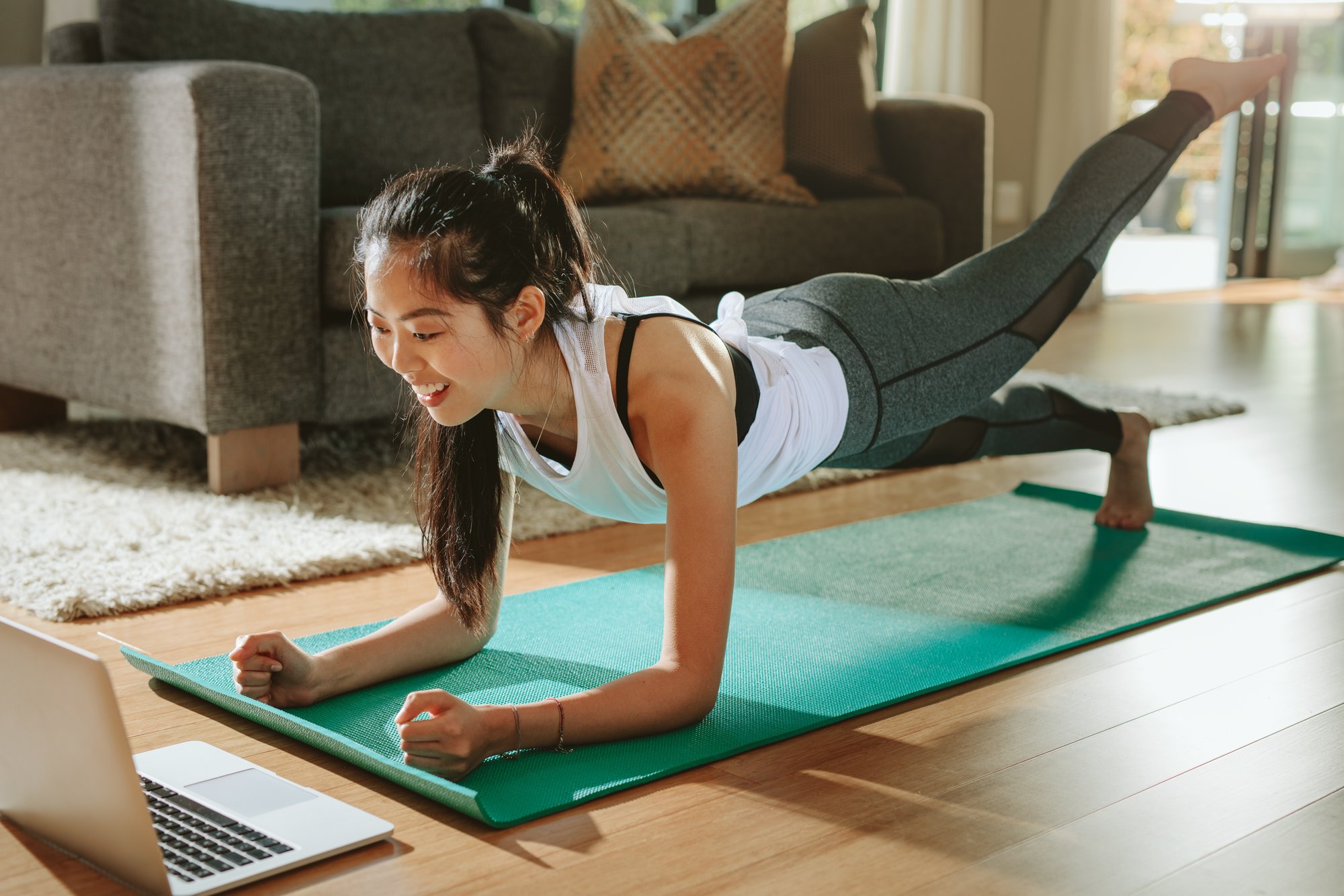 Woman in her living room doing an online workout on her laptop and using exercise as a lifestyle intervention to combat chronic pain from her endometriosis.