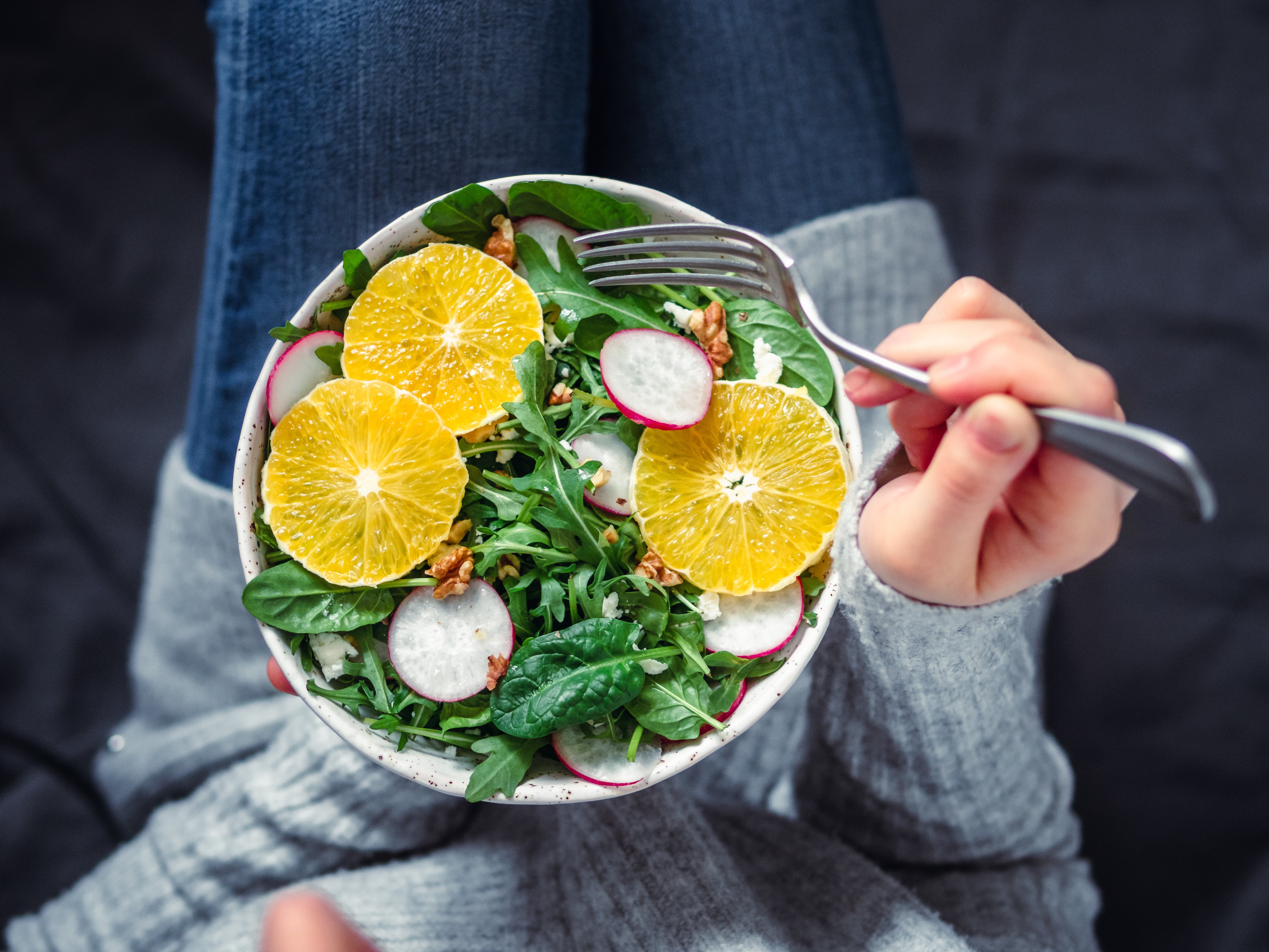 Top view of a women holding a colorful orange salad, linking healthy food to reduced inflammation.