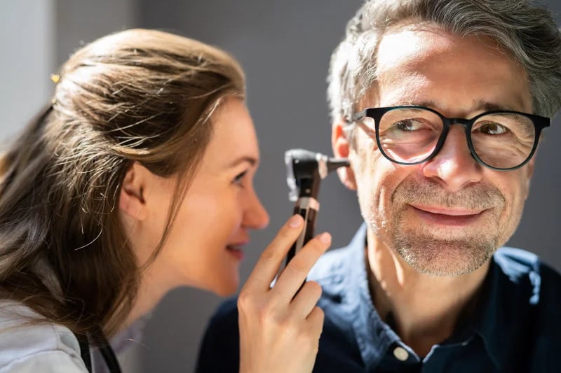 Woman functional medicine doctor checking the ears of a male patient for hearing loss