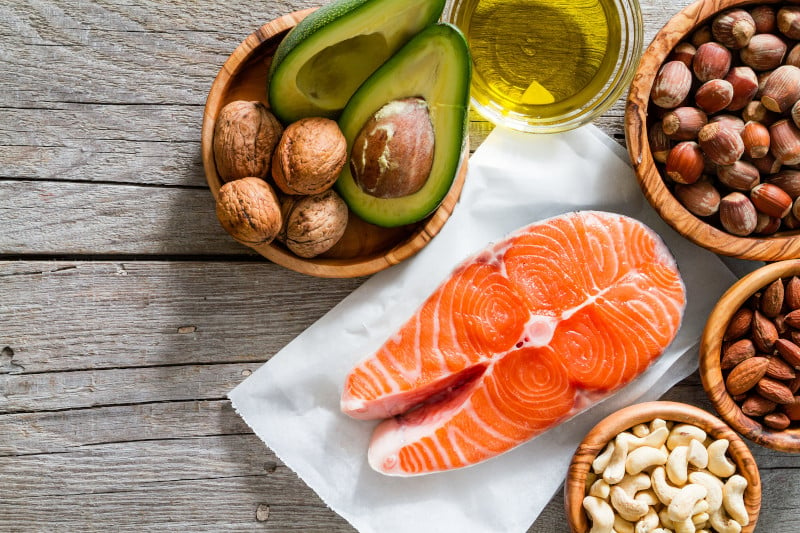 Flat lay of healthy fat sources, salmon, various nuts, and avocado that make up the ketogenic diet, one of the functional medicine treatments for chronic migraines.