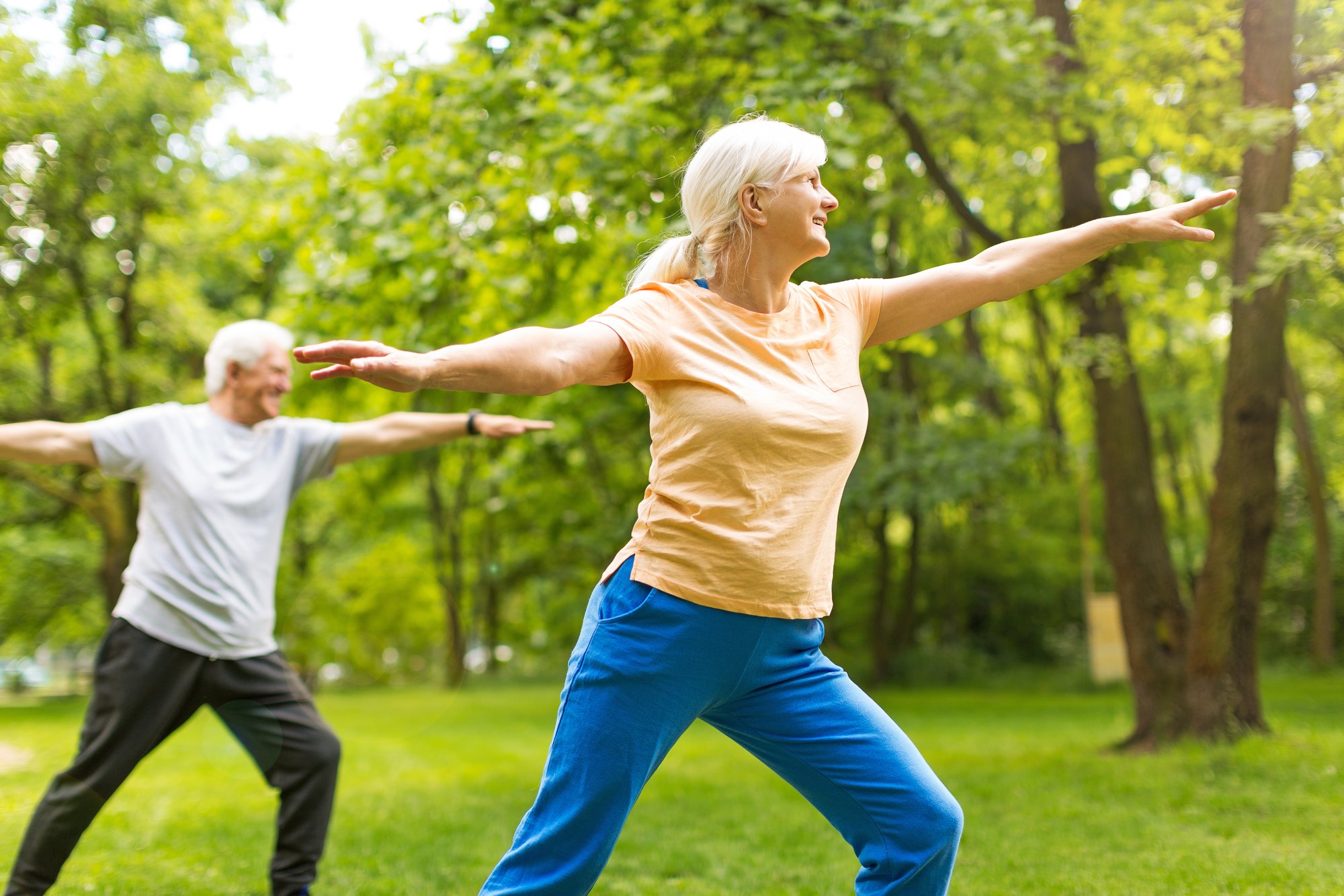 Elderly couple doing yoga in the park to increase their gut health through hormone balancing therapies.