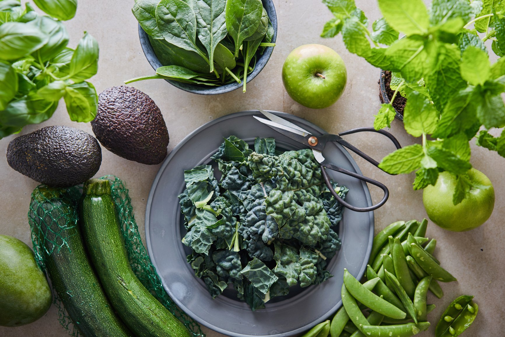 Flat lay of fresh green fruits, vegetables, and herbs that decrease inflammation and help reproductive health.
